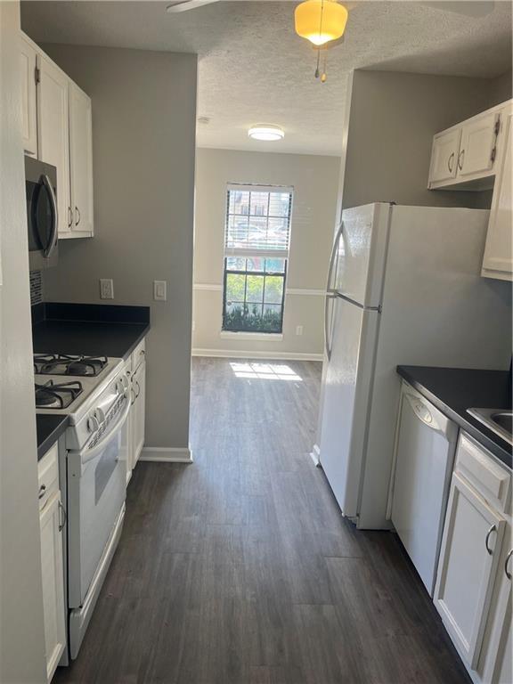 kitchen featuring white appliances, dark countertops, and white cabinets