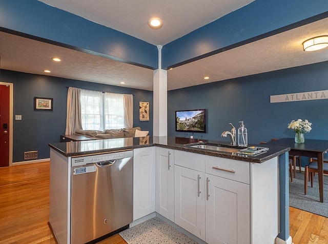 kitchen with stainless steel dishwasher, dark stone counters, sink, and white cabinets