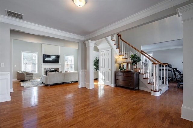 unfurnished living room featuring decorative columns, wood-type flooring, and ornamental molding