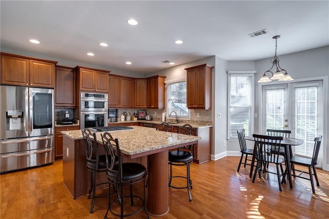 kitchen featuring appliances with stainless steel finishes, backsplash, a center island, light stone counters, and wood-type flooring