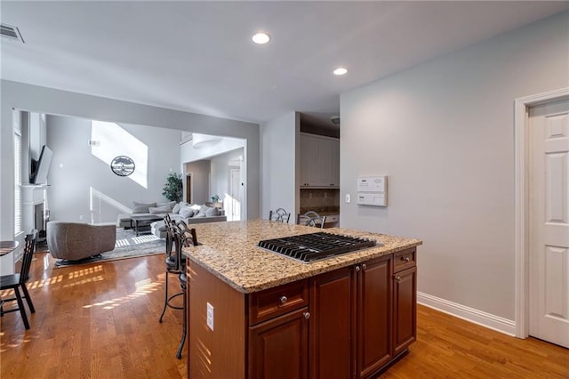 kitchen featuring light hardwood / wood-style flooring, a center island, light stone counters, tasteful backsplash, and a kitchen bar