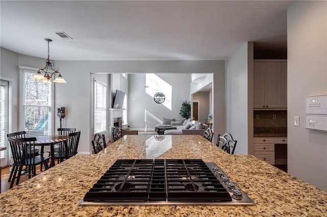 kitchen with black gas stovetop, light stone counters, a kitchen breakfast bar, and decorative backsplash