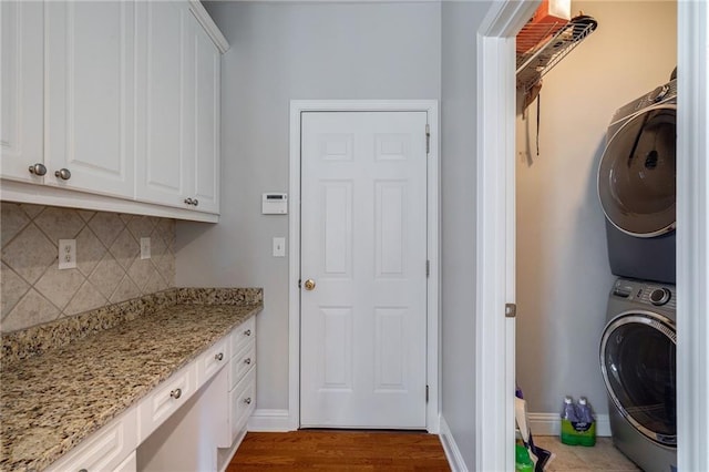 laundry room with cabinets, stacked washer / drying machine, and light wood-type flooring