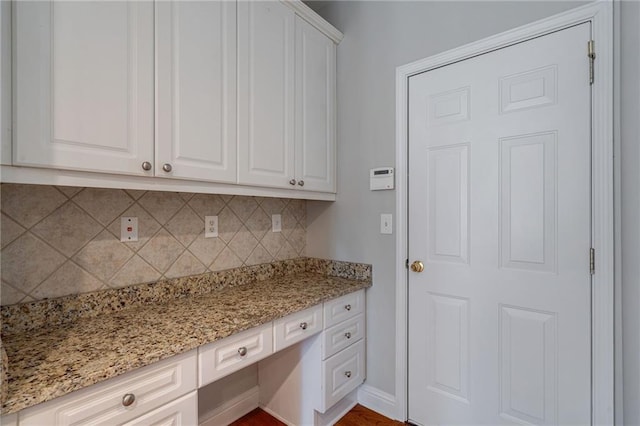 kitchen with white cabinetry, backsplash, light stone counters, and built in desk