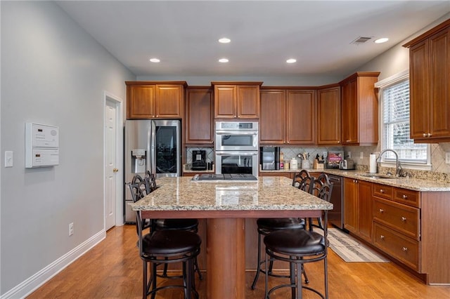 kitchen with sink, a breakfast bar, appliances with stainless steel finishes, light stone counters, and a kitchen island