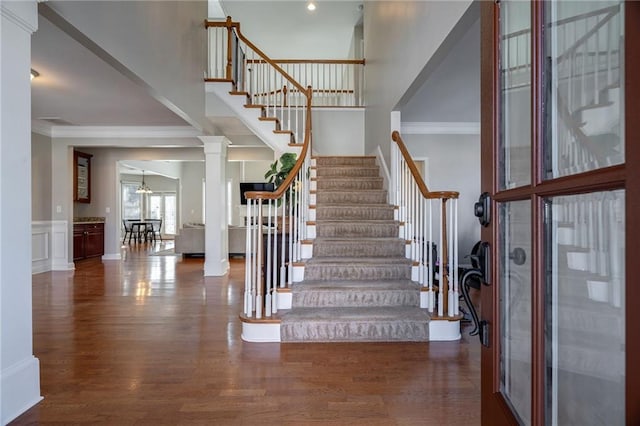 staircase featuring ornate columns, crown molding, and wood-type flooring