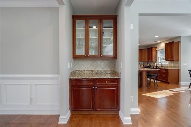 bar featuring sink, backsplash, light stone counters, and light hardwood / wood-style flooring