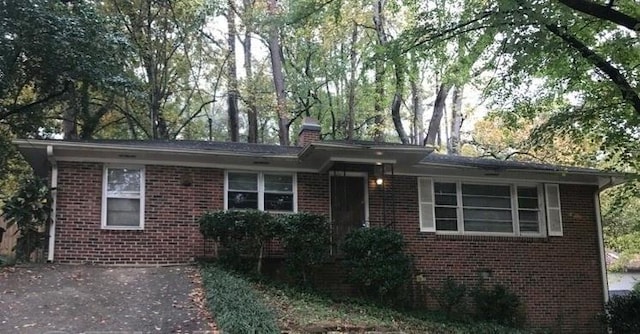 view of front of home featuring brick siding, a chimney, and view of wooded area