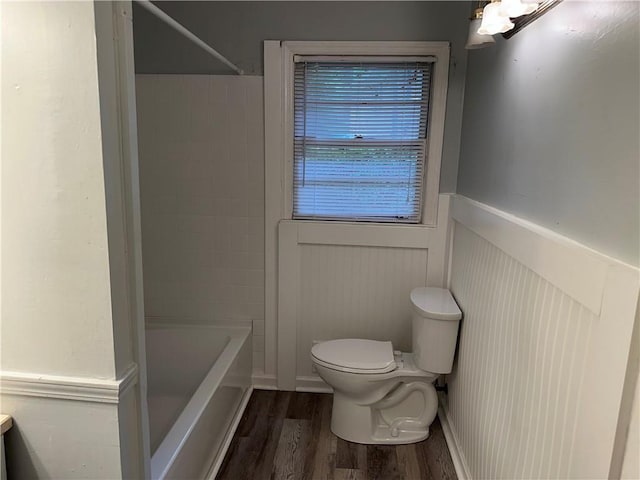 bathroom featuring wainscoting, wood finished floors, toilet, and  shower combination