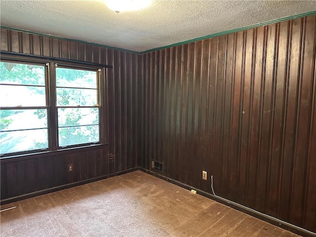 unfurnished room featuring a textured ceiling, light colored carpet, and wooden walls