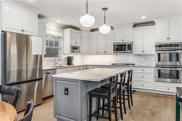 kitchen with light wood-type flooring, light countertops, appliances with stainless steel finishes, white cabinetry, and a sink