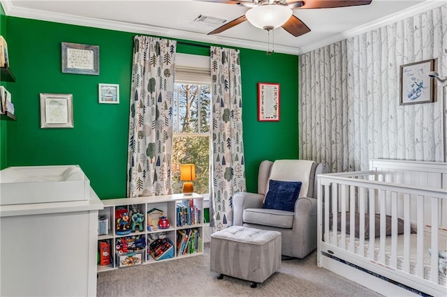 carpeted bedroom featuring visible vents, a crib, ornamental molding, a ceiling fan, and an accent wall