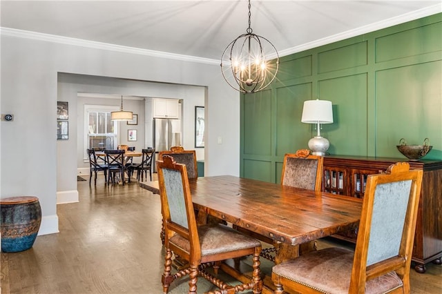 dining space featuring crown molding, baseboards, a chandelier, wood finished floors, and a decorative wall