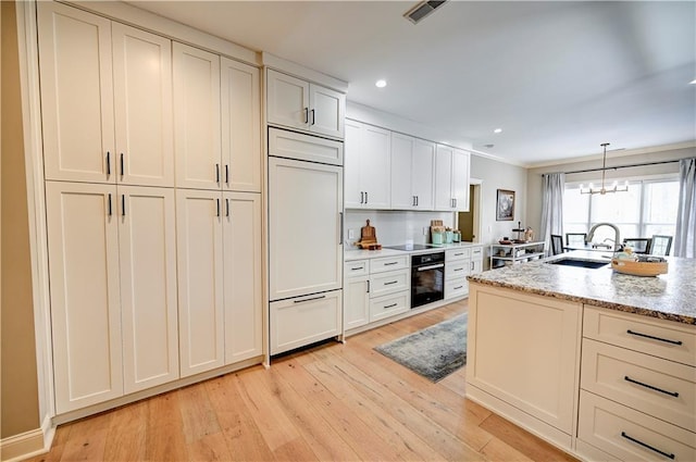 kitchen featuring hanging light fixtures, light stone counters, crown molding, black appliances, and light wood-type flooring