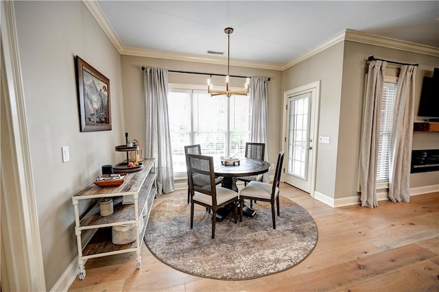 dining area with ornamental molding, an inviting chandelier, and light hardwood / wood-style flooring