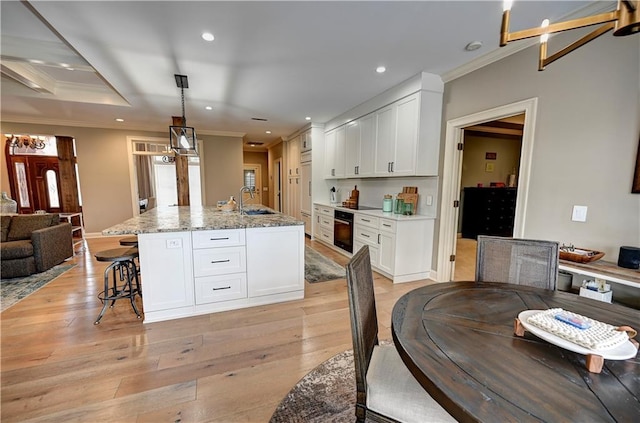 kitchen featuring light stone countertops, light wood-type flooring, a kitchen island with sink, black appliances, and white cabinets