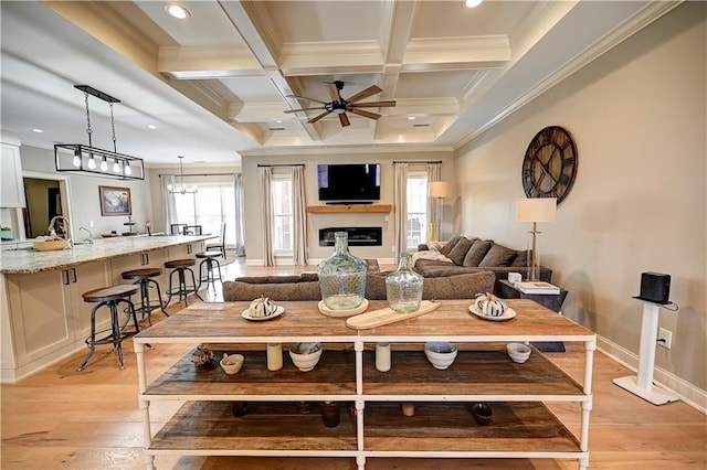 living room with beam ceiling, coffered ceiling, crown molding, light hardwood / wood-style floors, and ceiling fan with notable chandelier