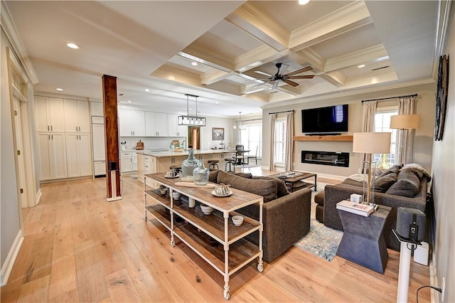 living room with beamed ceiling, light wood-type flooring, ceiling fan with notable chandelier, and coffered ceiling