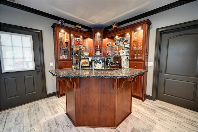 bar with dark stone countertops, sink, light hardwood / wood-style floors, and ornamental molding