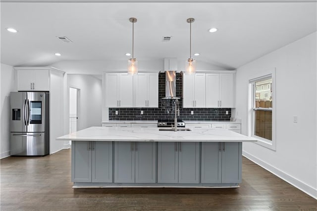 kitchen with wall chimney range hood, stainless steel fridge, white cabinets, and a center island with sink