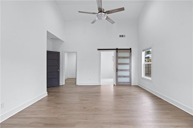 unfurnished living room featuring a high ceiling, ceiling fan, a barn door, and light hardwood / wood-style floors