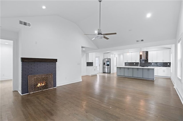 unfurnished living room featuring ceiling fan, high vaulted ceiling, dark hardwood / wood-style floors, and a fireplace