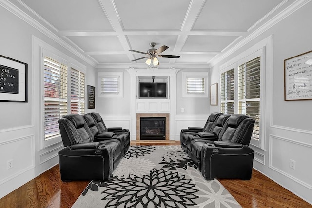 living room with dark wood-type flooring, coffered ceiling, ornamental molding, a tile fireplace, and ceiling fan