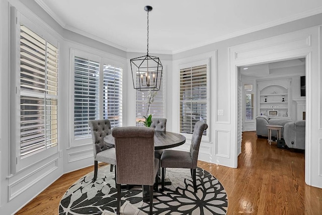 dining room with ornamental molding, a chandelier, wood-type flooring, and built in features