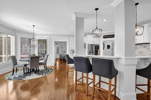 kitchen featuring an inviting chandelier, stainless steel refrigerator with ice dispenser, ornamental molding, white cabinets, and kitchen peninsula