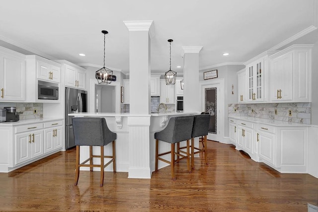 kitchen featuring appliances with stainless steel finishes, a breakfast bar, decorative light fixtures, white cabinets, and dark hardwood / wood-style flooring