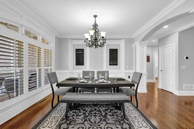 dining space with ornate columns, crown molding, dark wood-type flooring, and an inviting chandelier