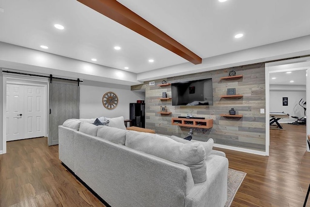 living room with beam ceiling, dark hardwood / wood-style floors, a barn door, and wood walls