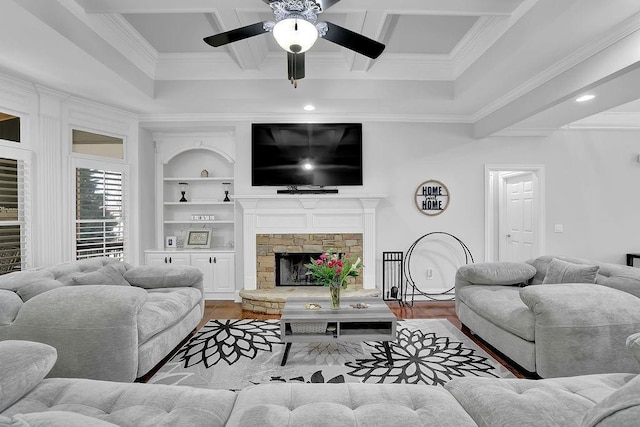 living room featuring crown molding, built in shelves, a stone fireplace, and light wood-type flooring