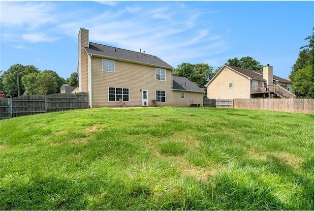 rear view of property featuring a fenced backyard, a yard, and a chimney