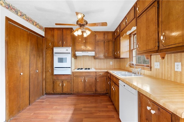 kitchen with brown cabinets, a warming drawer, a sink, white appliances, and under cabinet range hood