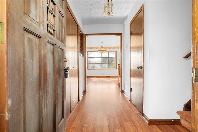 hall featuring light wood finished floors, visible vents, baseboards, stairs, and a textured ceiling