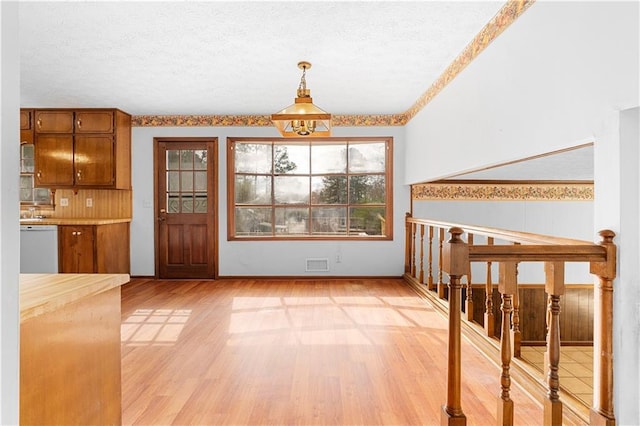 unfurnished dining area with light wood-style floors, visible vents, a textured ceiling, and stairs