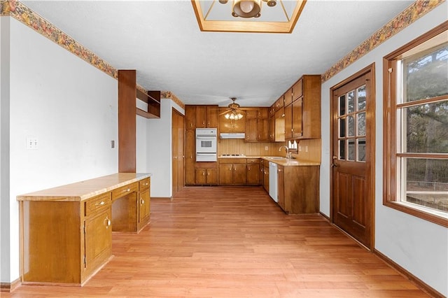 kitchen with light countertops, light wood-style flooring, brown cabinetry, a sink, and under cabinet range hood