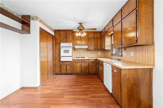 kitchen with brown cabinetry, white appliances, a sink, and under cabinet range hood