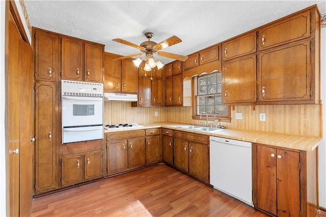 kitchen featuring white appliances, brown cabinetry, under cabinet range hood, a sink, and a warming drawer