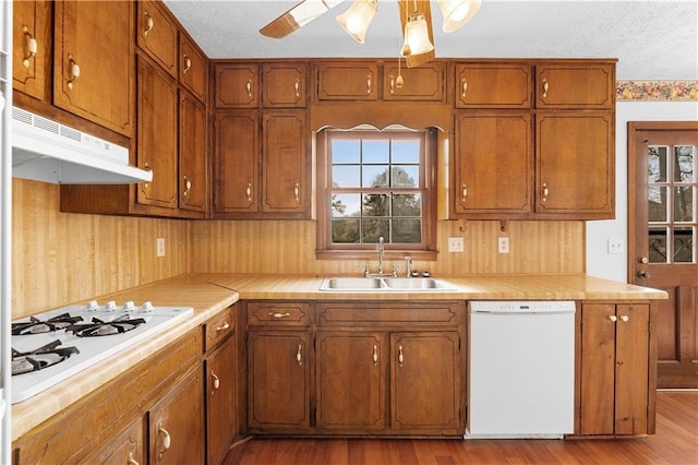 kitchen with brown cabinetry, white appliances, a sink, and under cabinet range hood