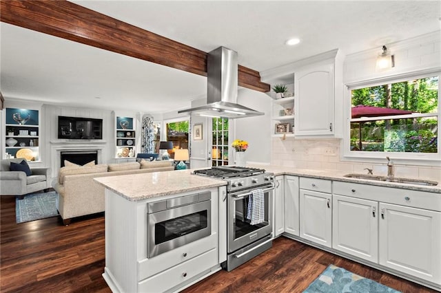 kitchen featuring stainless steel appliances, open shelves, wall chimney range hood, a sink, and a peninsula
