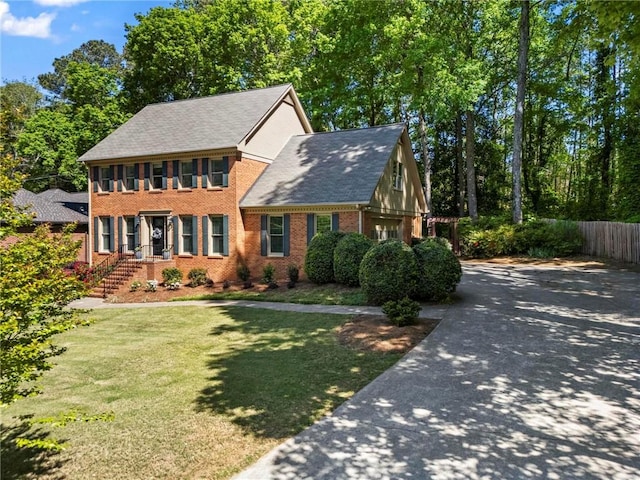 colonial inspired home featuring brick siding, fence, driveway, and a front yard