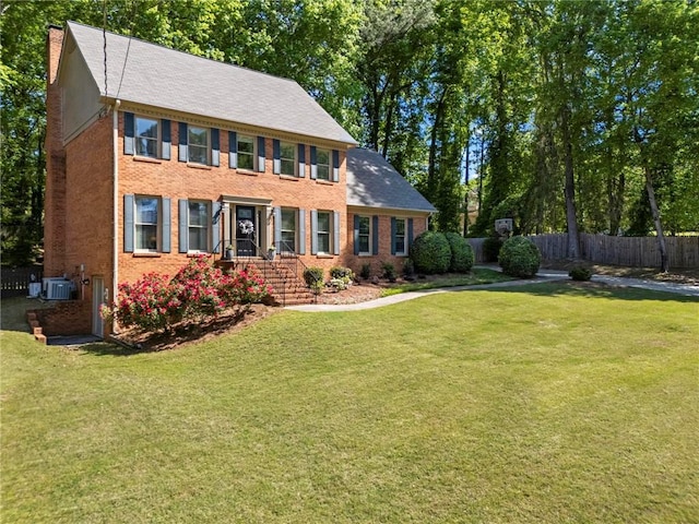 colonial-style house featuring a chimney, a front lawn, fence, cooling unit, and brick siding