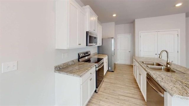 kitchen featuring appliances with stainless steel finishes, light hardwood / wood-style flooring, a center island with sink, light stone countertops, and white cabinetry