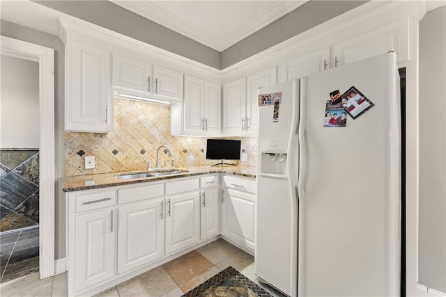 kitchen featuring light stone counters, a sink, white refrigerator with ice dispenser, backsplash, and white cabinetry