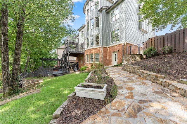 exterior space featuring brick siding, a wooden deck, fence, and a lawn