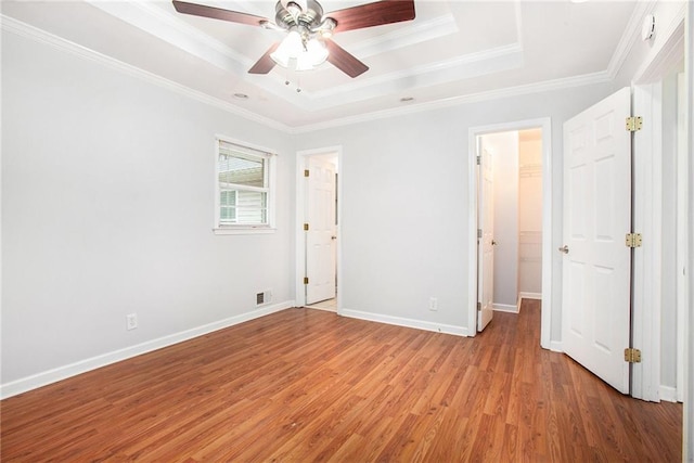 unfurnished bedroom with a raised ceiling, crown molding, a walk in closet, and light hardwood / wood-style flooring