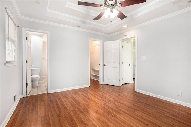 unfurnished bedroom with wood-type flooring, ornamental molding, a walk in closet, a tray ceiling, and ensuite bath