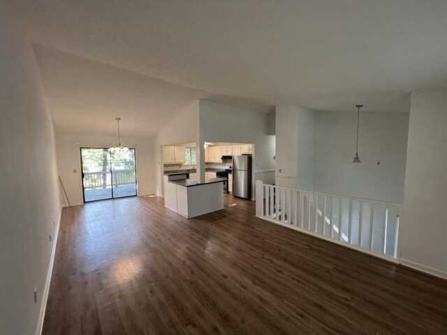 981 Dundee Dr, Lilburn, GA 30047 - unfurnished living room featuring vaulted ceiling, baseboards, a notable chandelier, and dark wood-style flooring